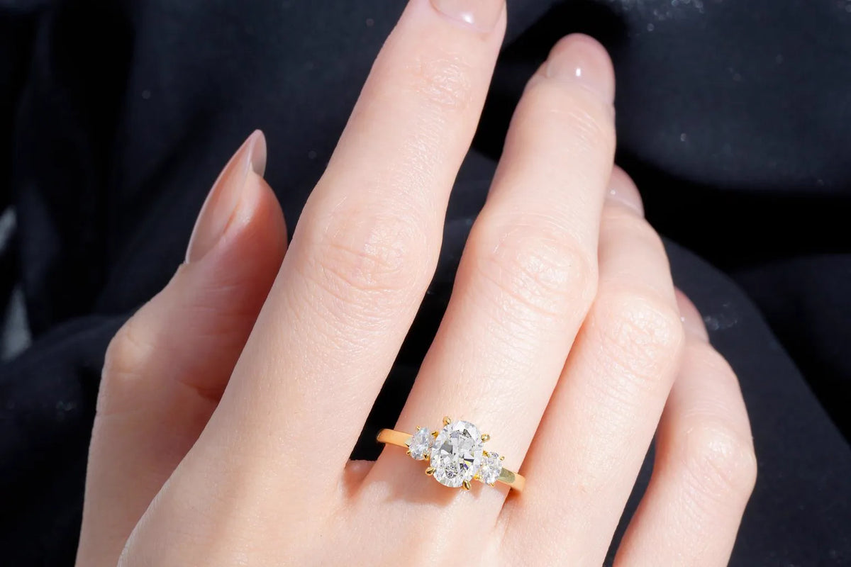 Oval three-stone moissanite ring shown on a hand in sunlight